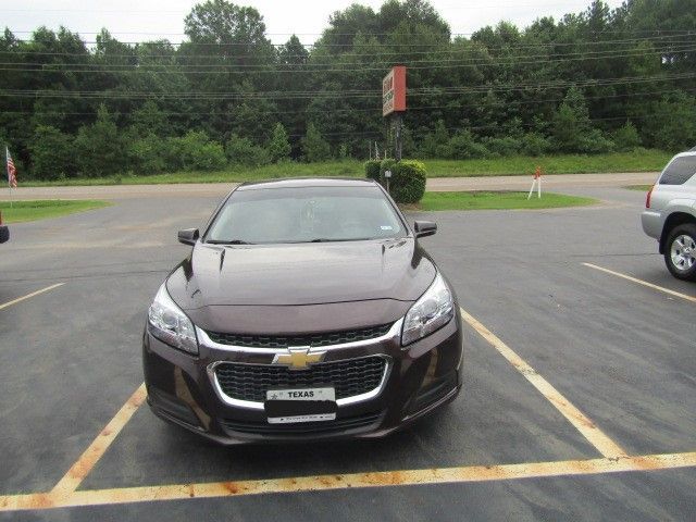 Dark brown Chevrolet sedan parked in a lot with trees in the background.