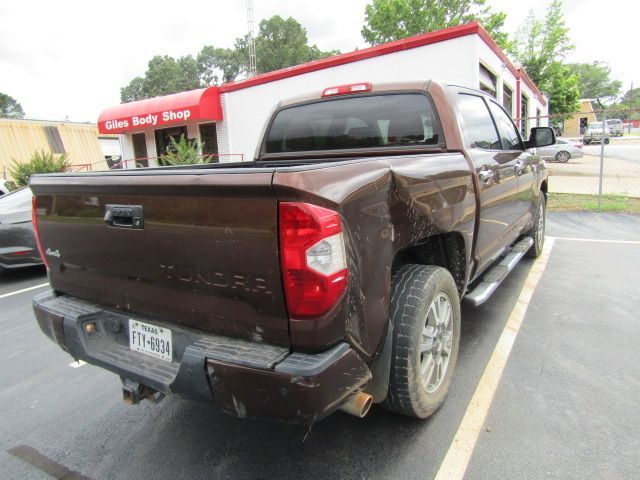Damaged brown pickup truck parked in a lot, rear corner crumpled near a red building