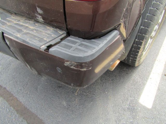 Close-up of a maroon car’s rear bumper with scuff marks, parked on asphalt near a white line.