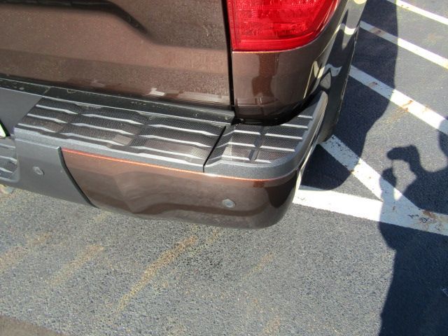 Rear corner of a brown SUV parked in a striped parking space, with a small dent on the bumper.