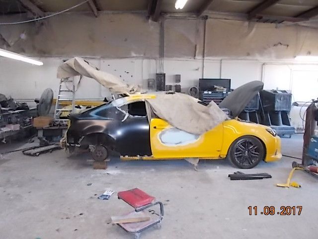 Yellow-and-black sports car under repair in a cluttered auto shop, covered with a tarp.
