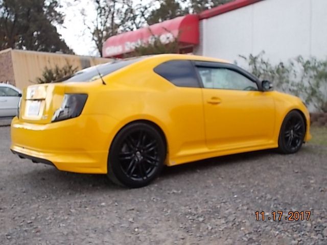 Yellow sports coupe parked on gravel beside a white building, viewed from the rear side.