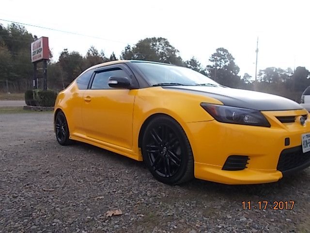 Yellow sports car parked on a gravel roadside under overcast skies
