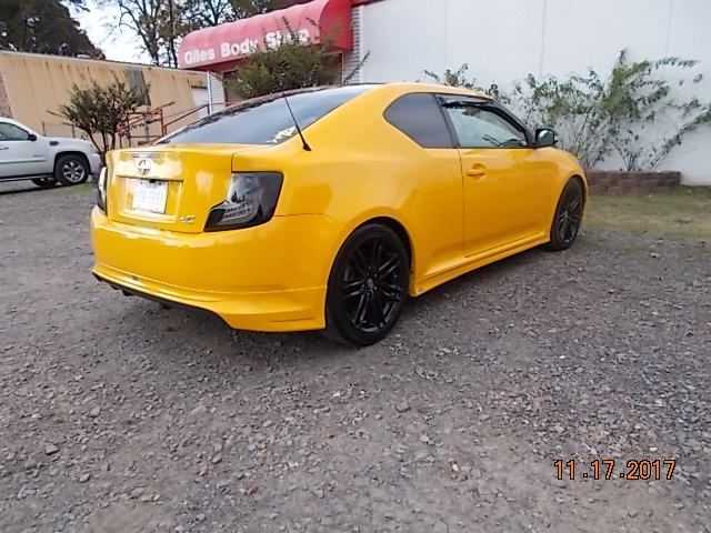 Yellow sports coupe parked on gravel beside a building, rear three-quarter view