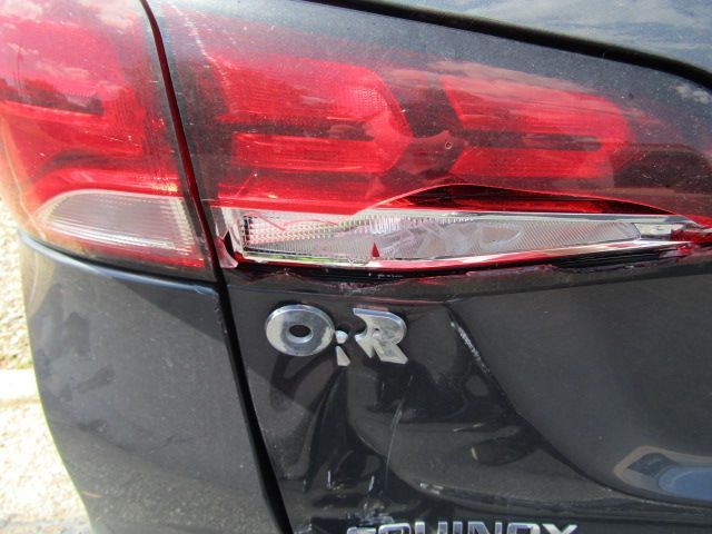 Close-up of a black car’s rear, showing a damaged taillight and dented bumper beside an “R” badge