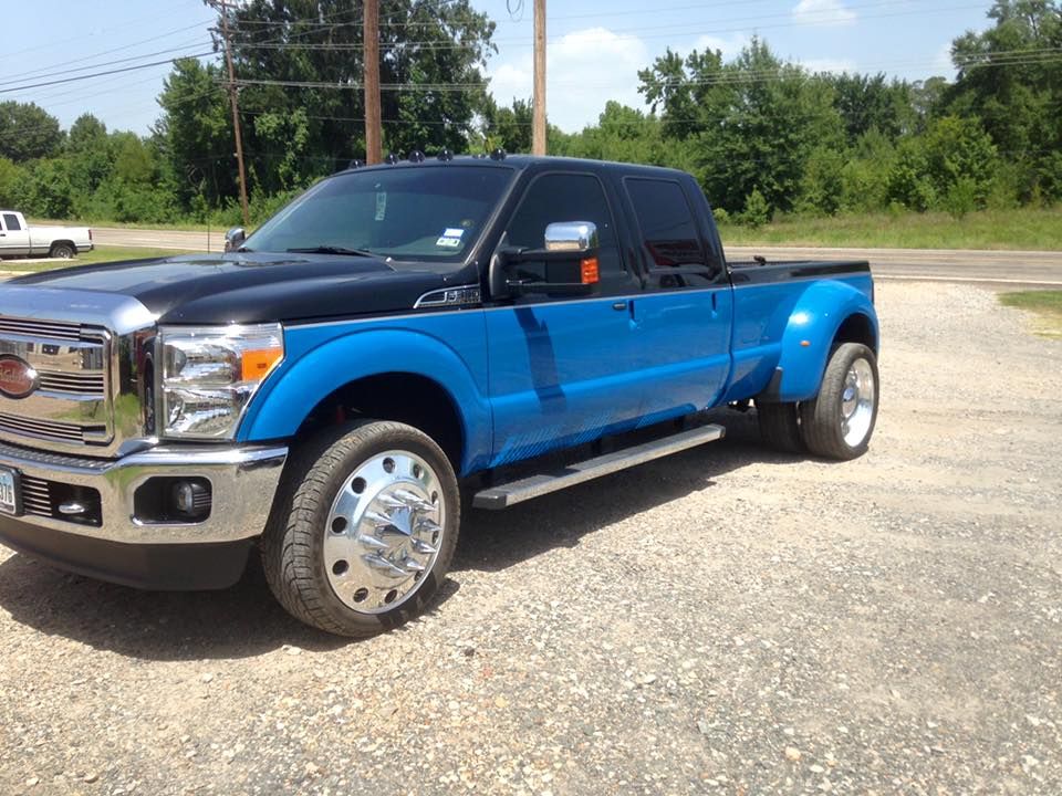 Blue and black Ford pickup truck parked on a gravel lot under a clear sky