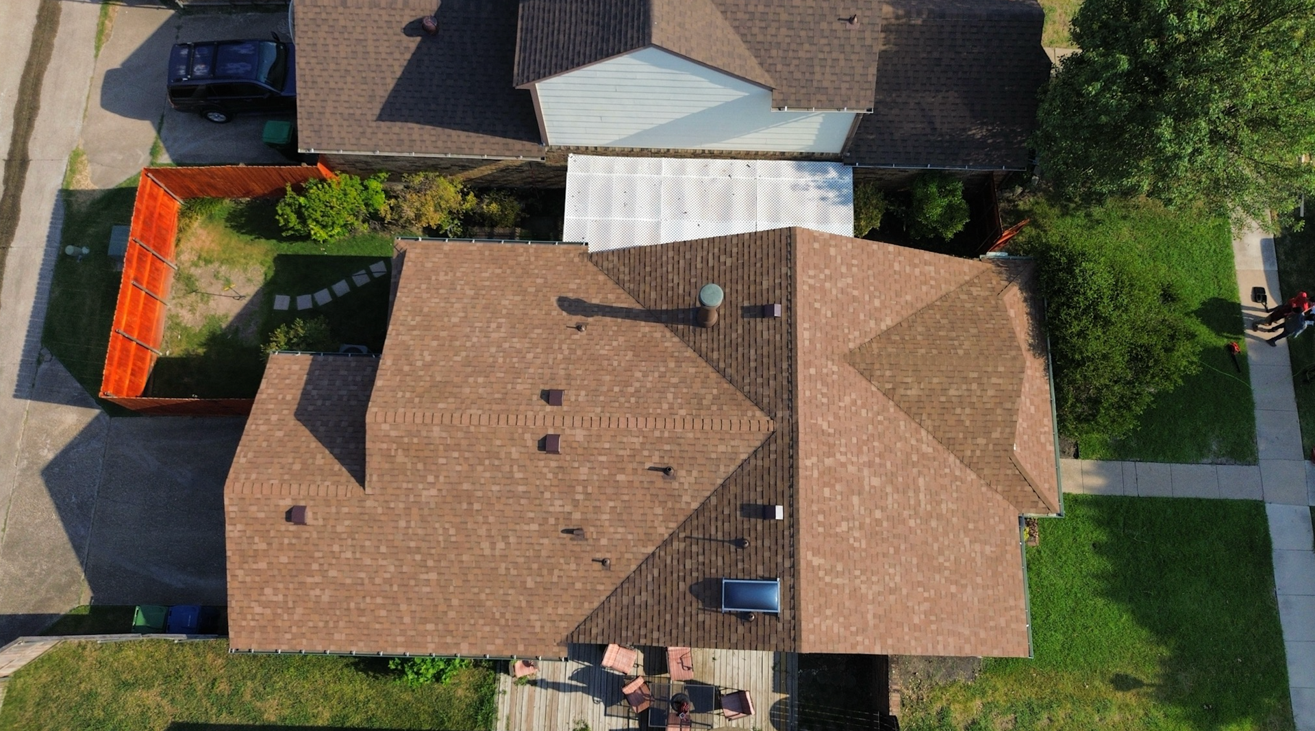 Overhead view of a house with a brown roof and surrounding yard, next to other buildings and a street.