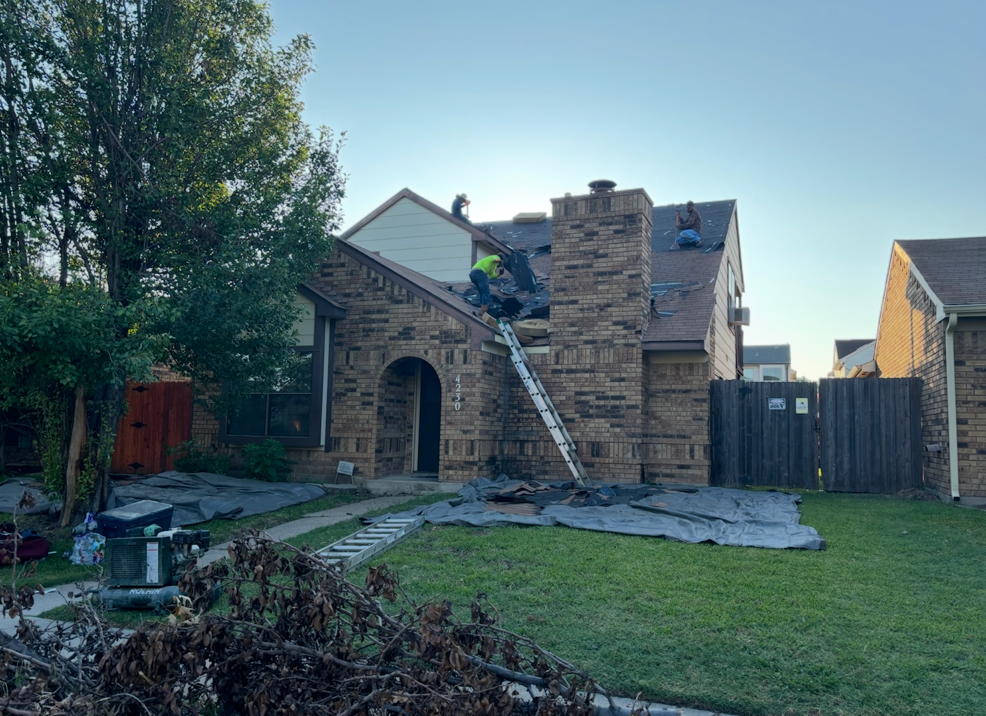 Roofers working on a house with a stone facade, using a ladder. Sunny, daytime setting.