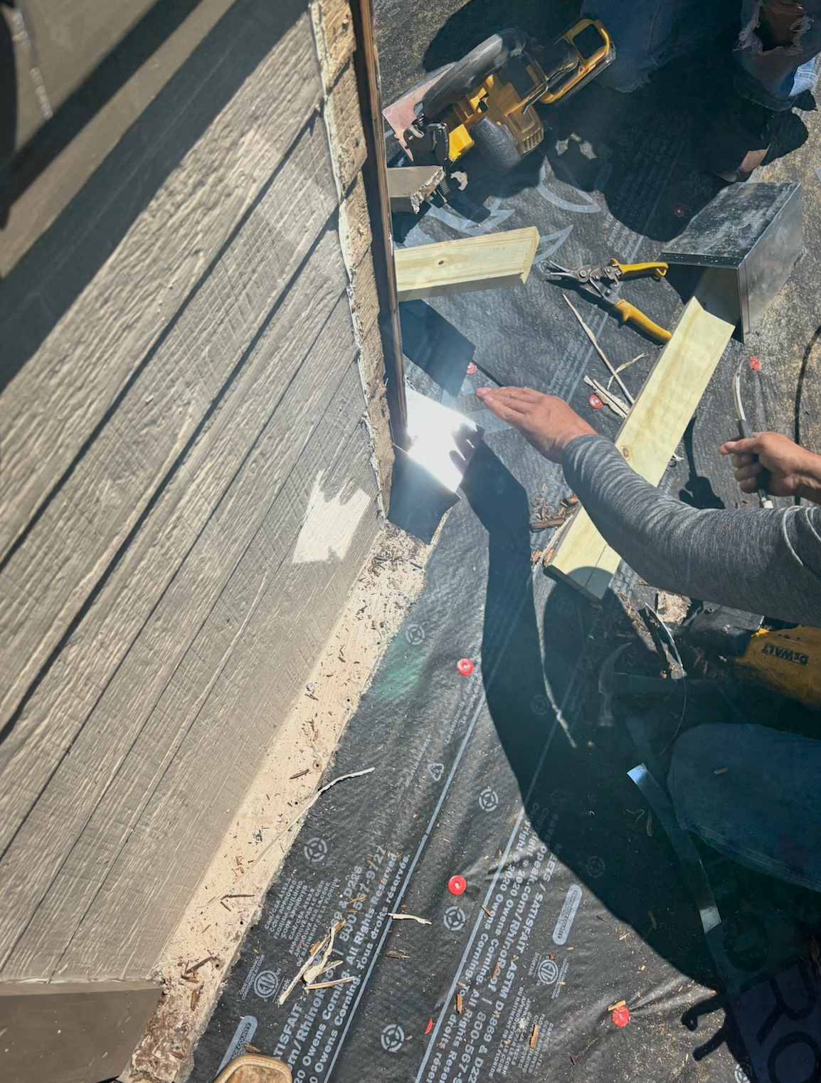 Person working on siding repair, using tools on a house exterior.