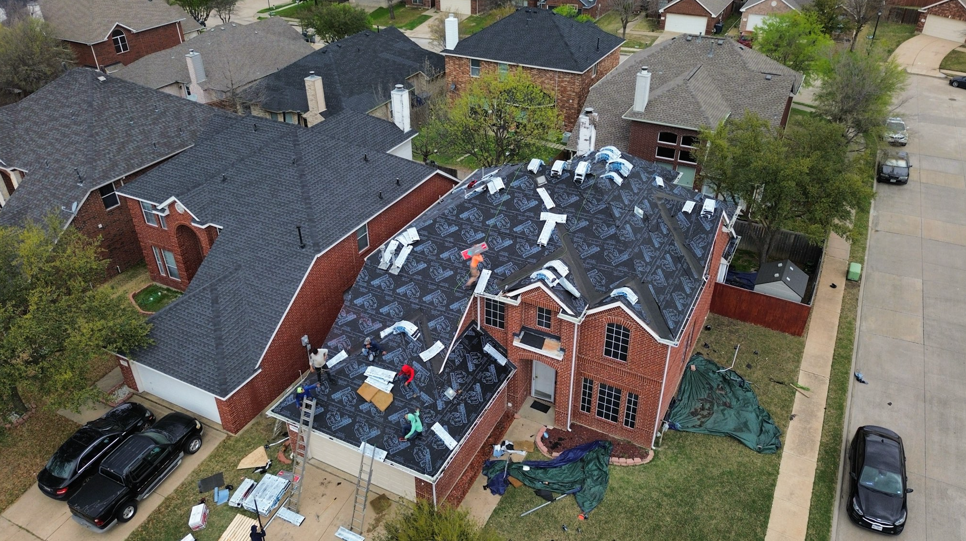 Aerial view of a home with roof being repaired. Workers, tools, and debris are visible on the roof.