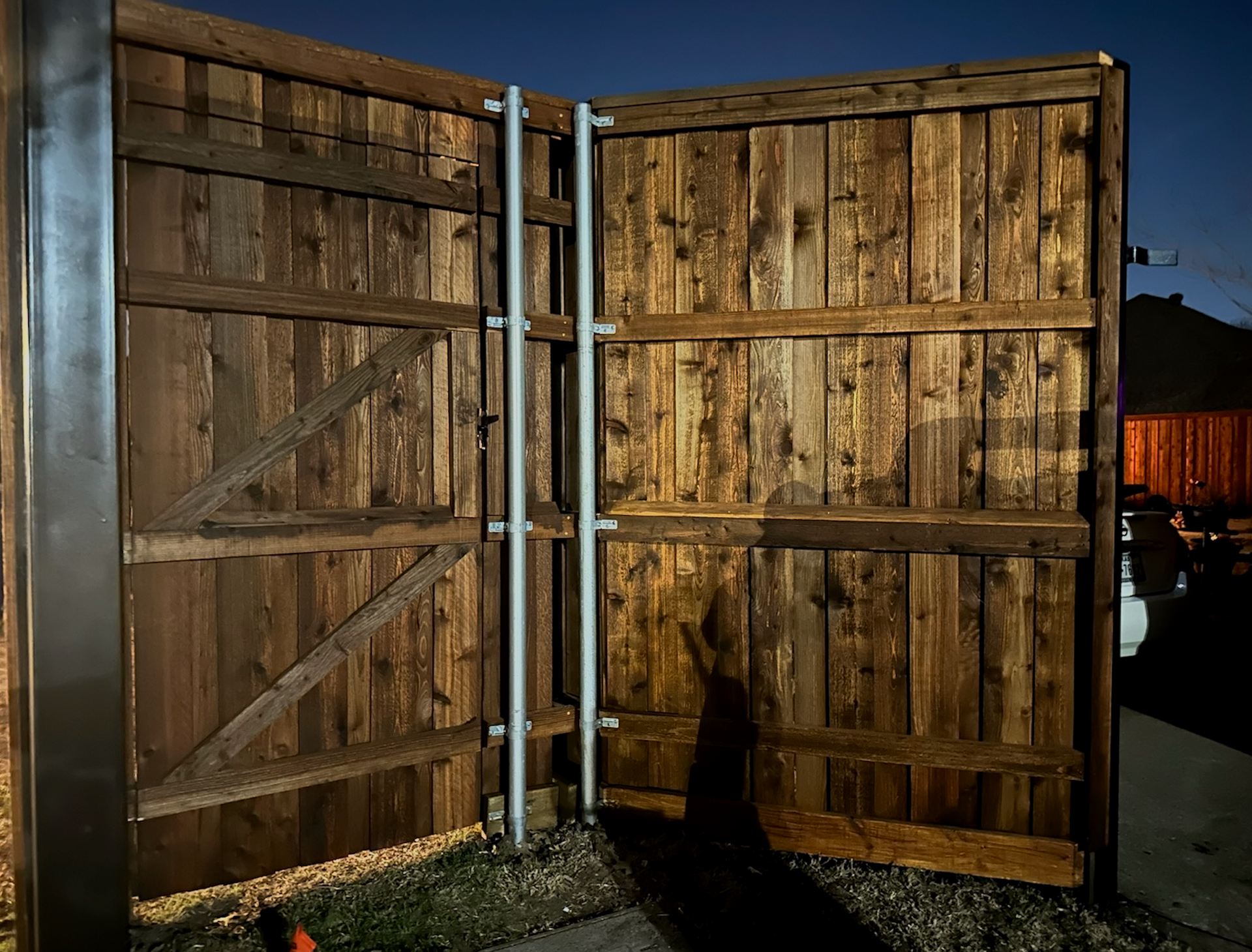 Wooden gate with vertical metal supports, ajar at night. Brown boards, dark setting.