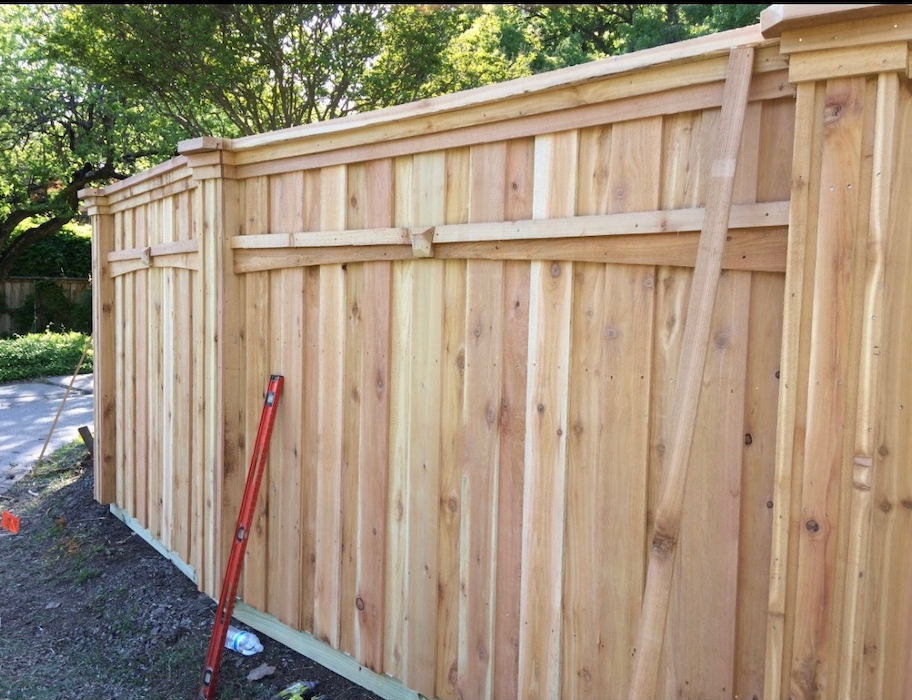 Wooden fence under construction outdoors, with vertical boards and decorative top.