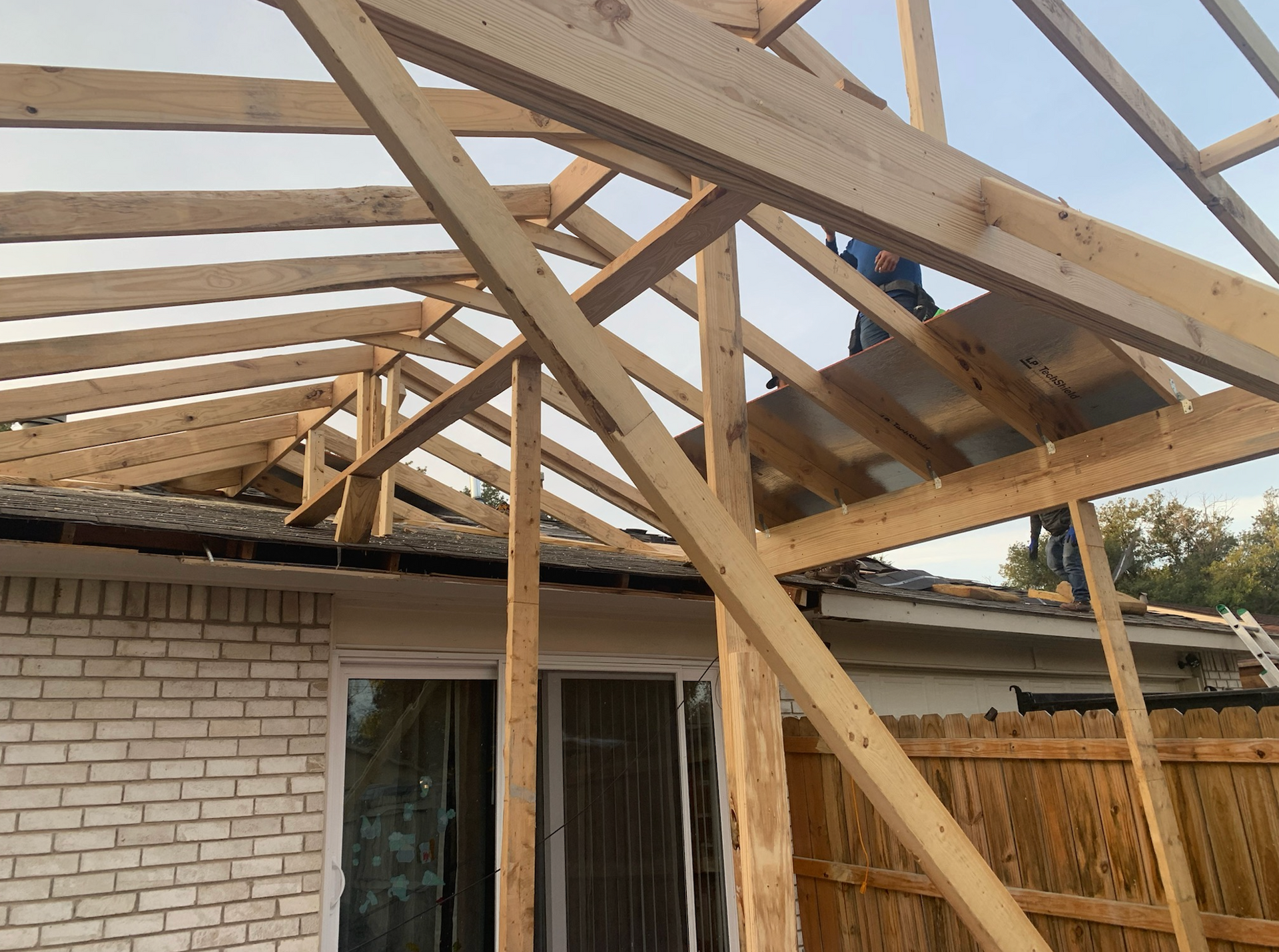 Construction of a new wooden roof structure over a brick building. Person working on the roof.