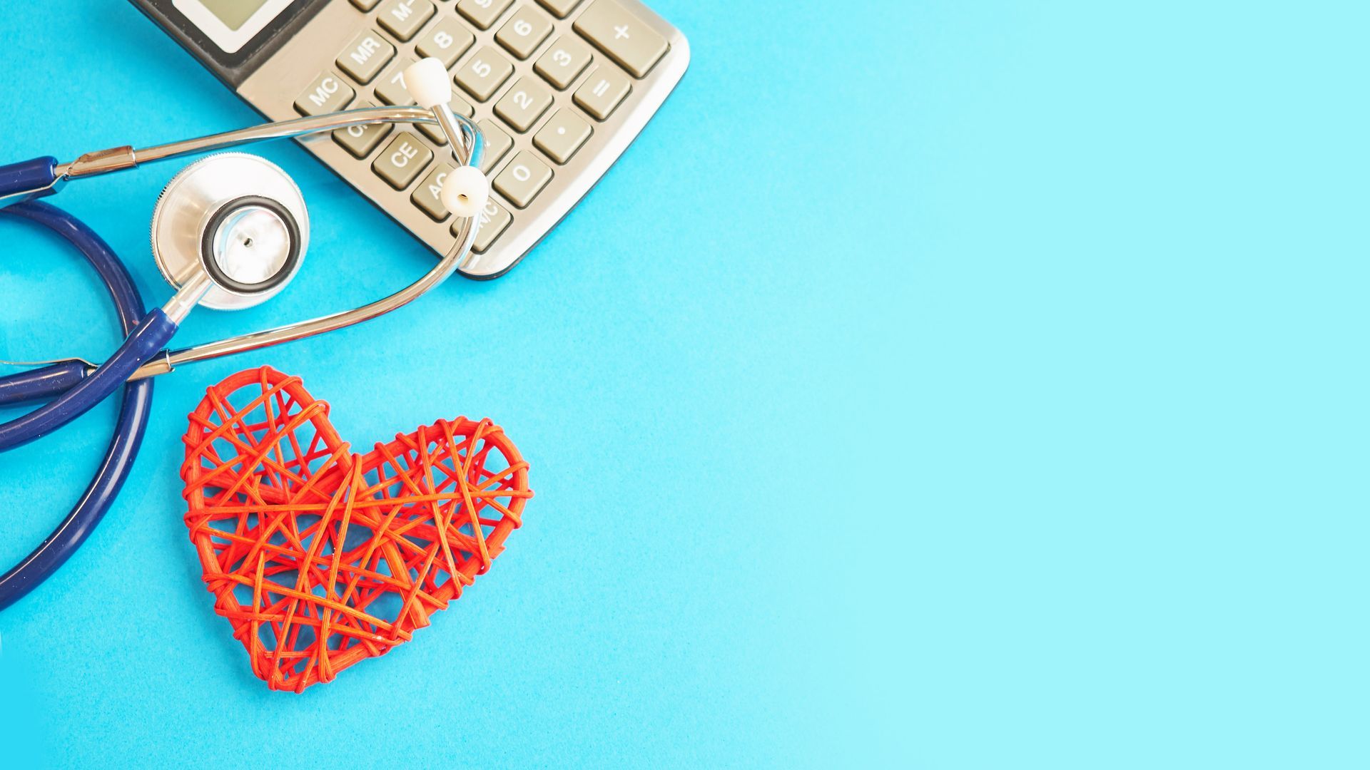 A stethoscope and a decorative red wire heart lie on a bright blue surface next to a calculator.