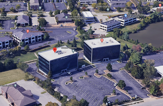 Aerial view of two office buildings beside a parking lot and waterway.