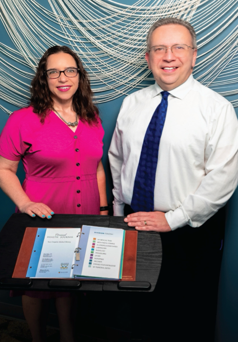 Two professionals standing behind an open binder on a podium in front of a blue abstract wall