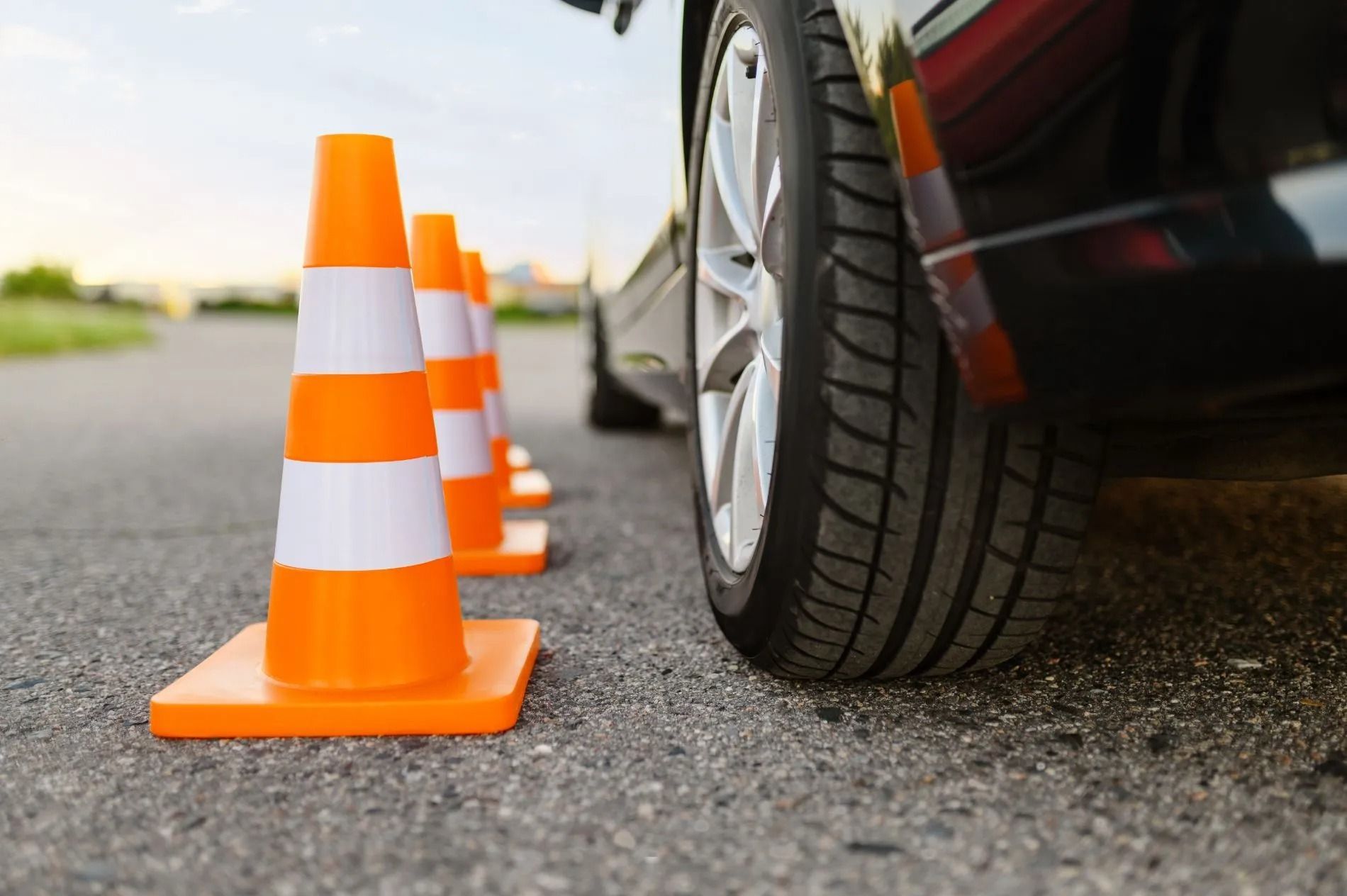Coni stradali arancioni allineati vicino a uno pneumatico d'auto sull'asfalto.
