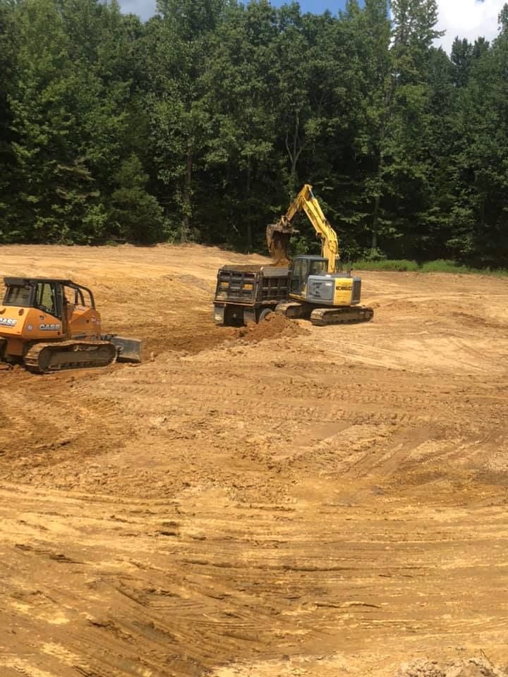 Yellow excavator loading dirt into a dump truck at a construction site with a yellow bulldozer parked nearby.