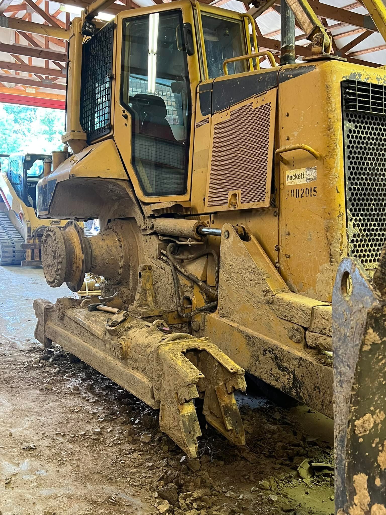A muddy yellow bulldozer missing its tracks sits parked inside a large, open-sided metal shed.