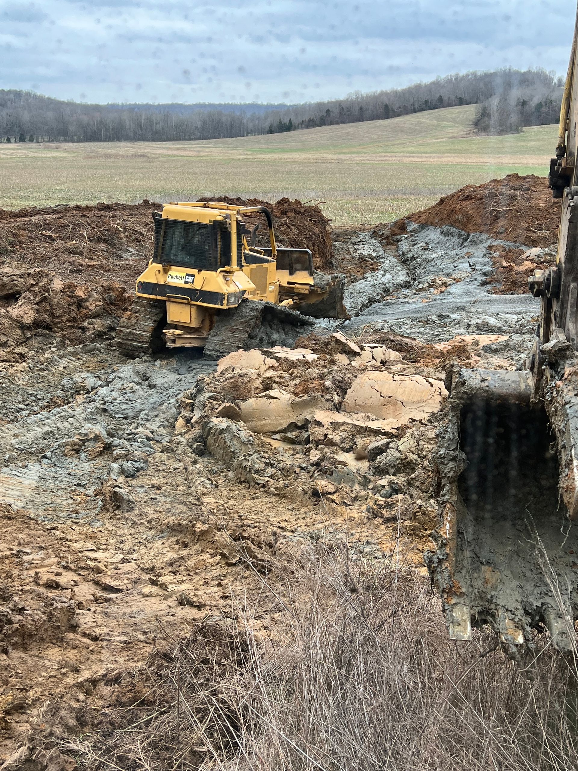A yellow bulldozer operates on a muddy construction site under a cloudy sky.