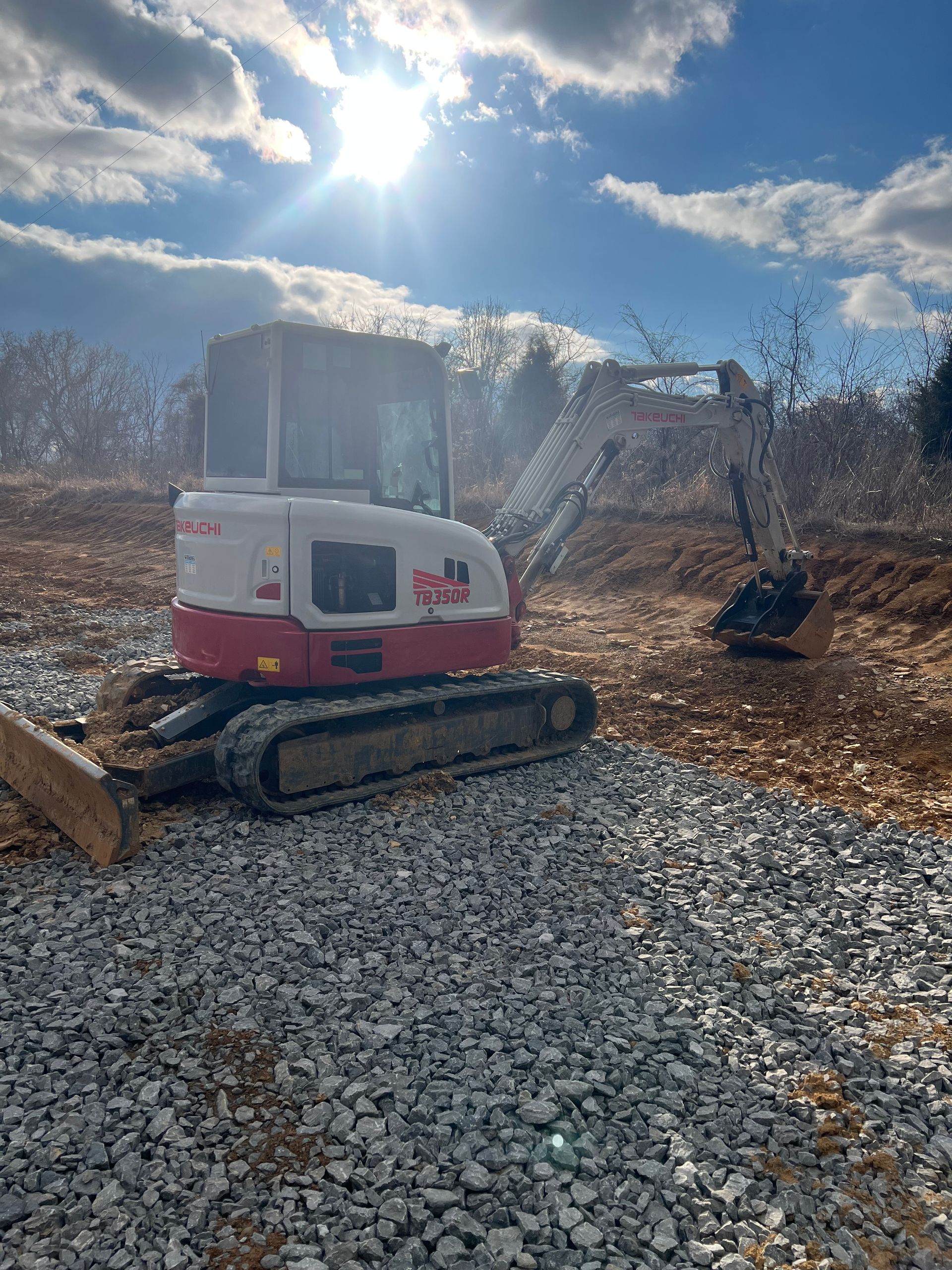A white and red Takeuchi excavator parked on a gravel construction site under a bright sun.