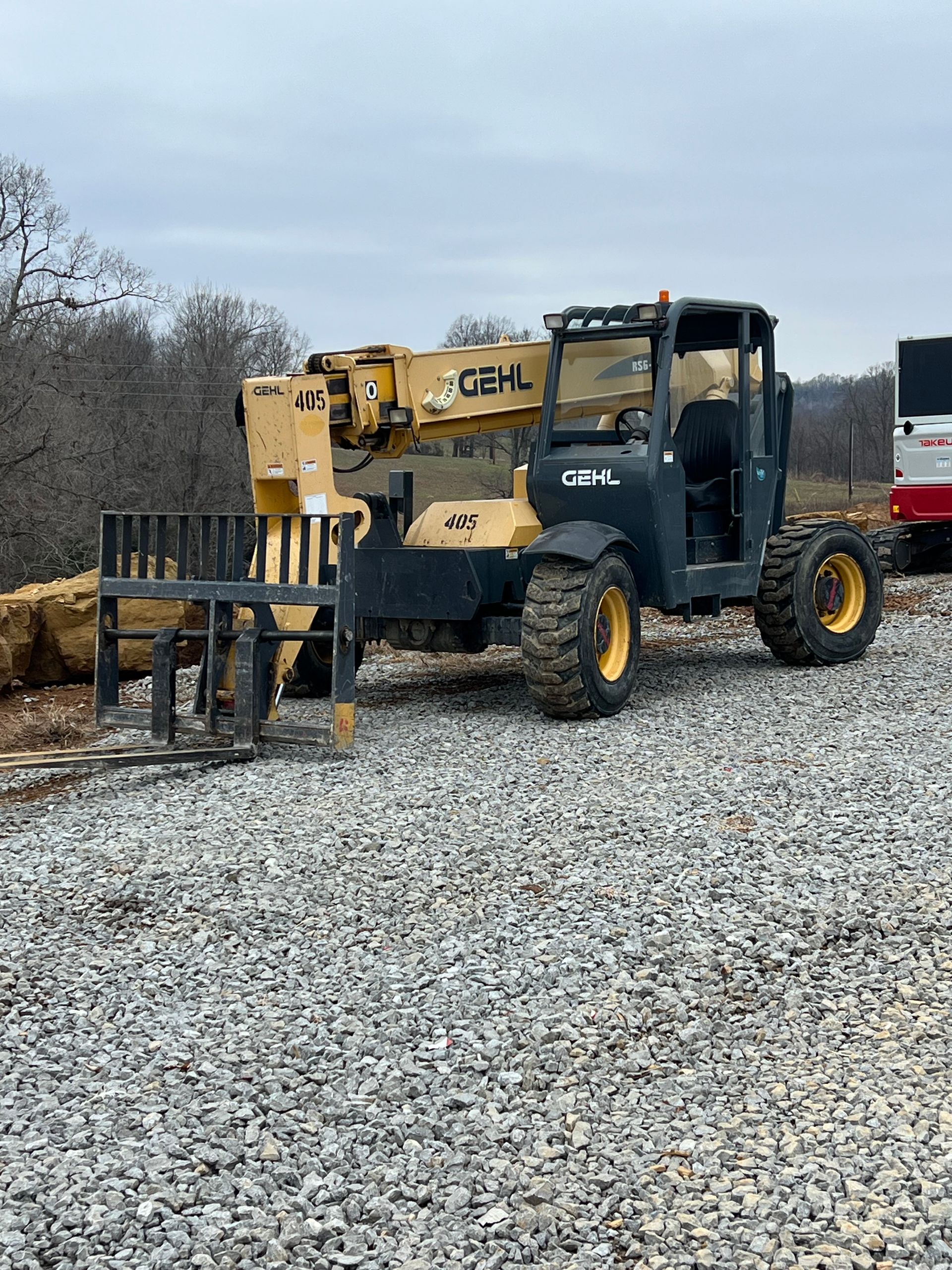A yellow and black telehandler parked on a gravel construction site under a cloudy sky.
