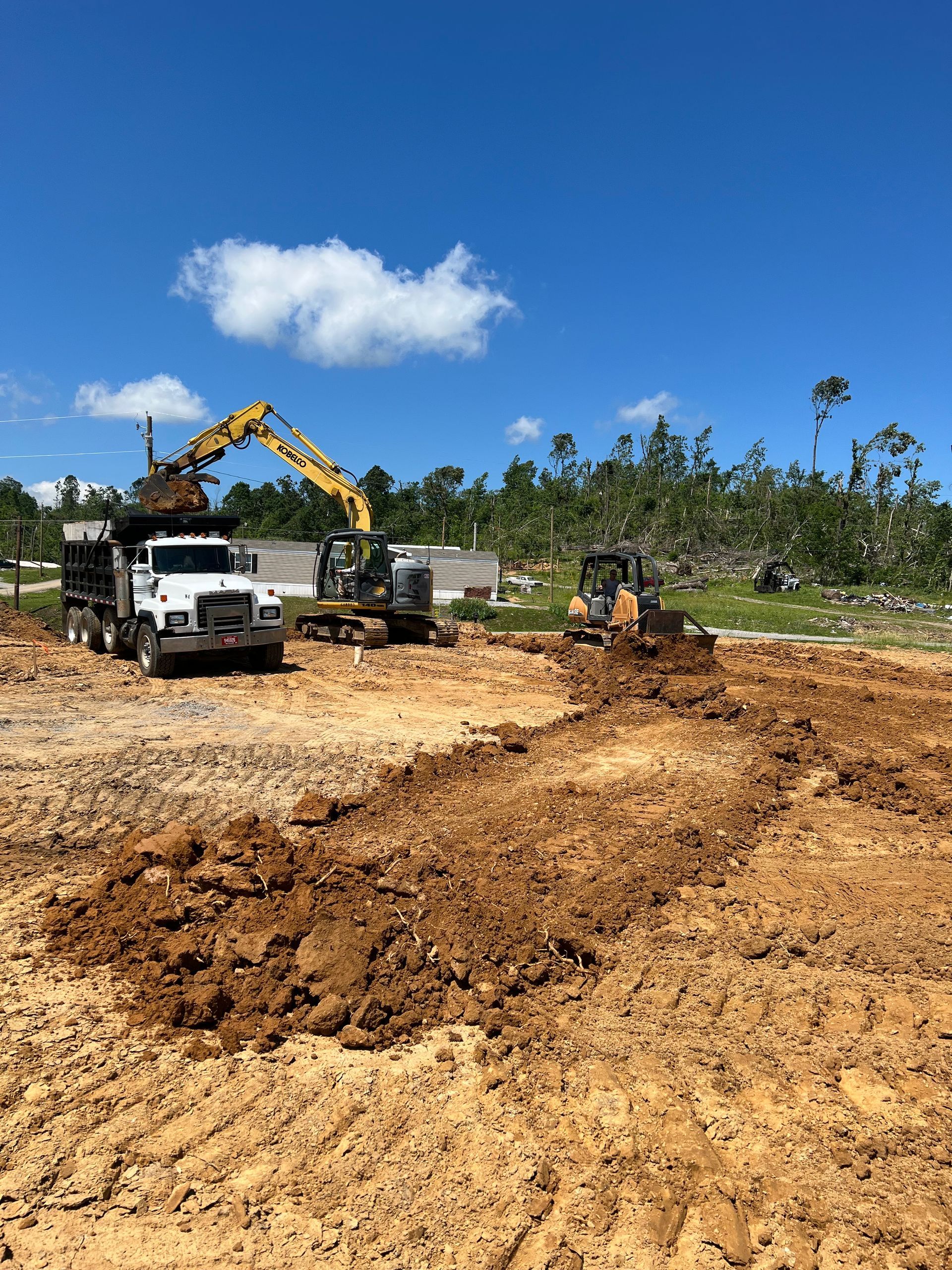 An excavator loads dirt into a dump truck at a construction site with a bulldozer nearby under a clear blue sky.
