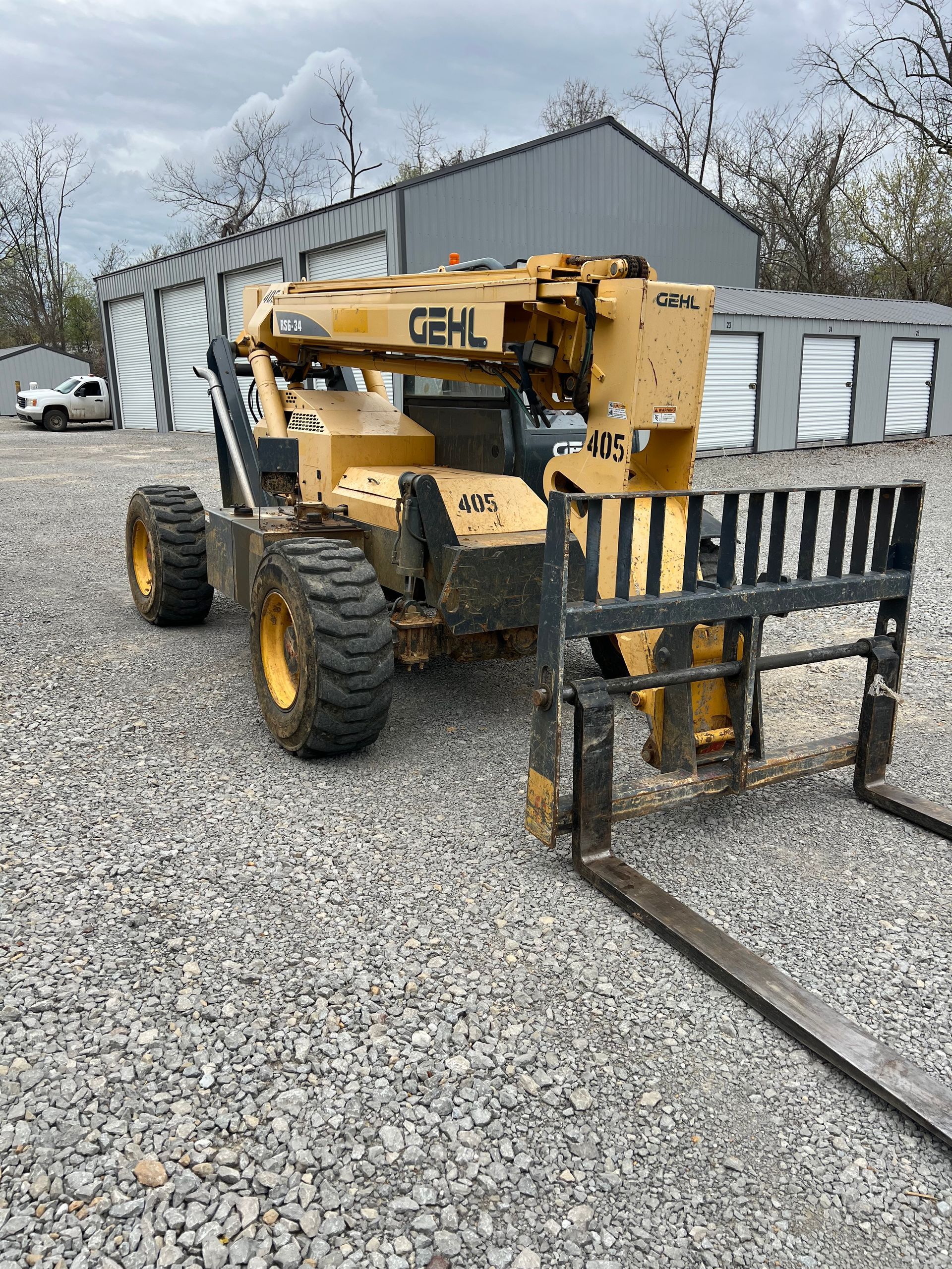 A yellow GEHL telehandler forklift sits on a gravel lot in front of a metal storage building.