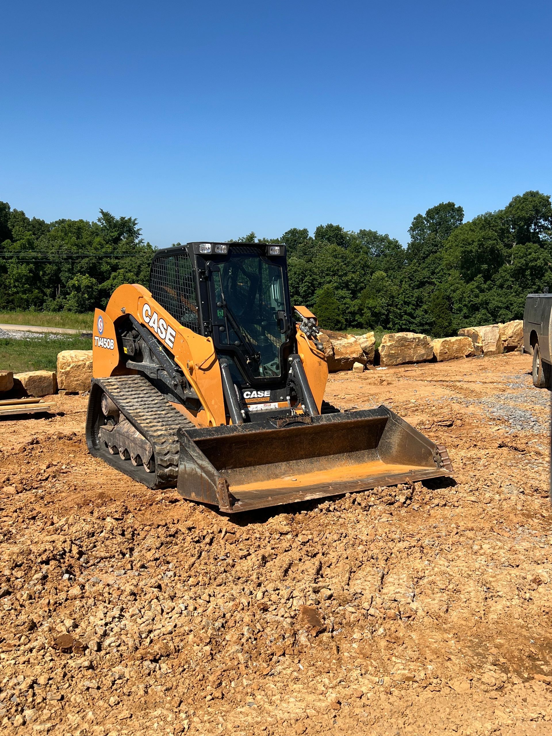 A yellow compact track loader with a front bucket parked on a dirt construction site under a clear blue sky.