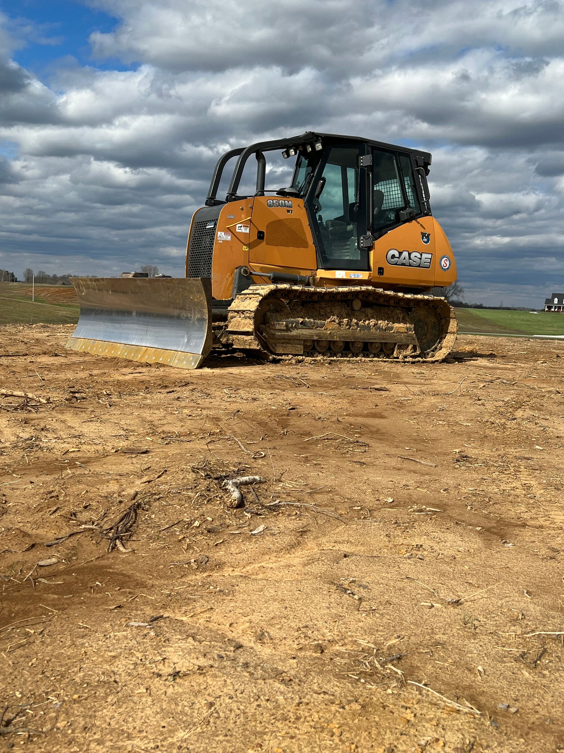 A yellow Case bulldozer sits on a dirt-covered field under a blue, cloudy sky.