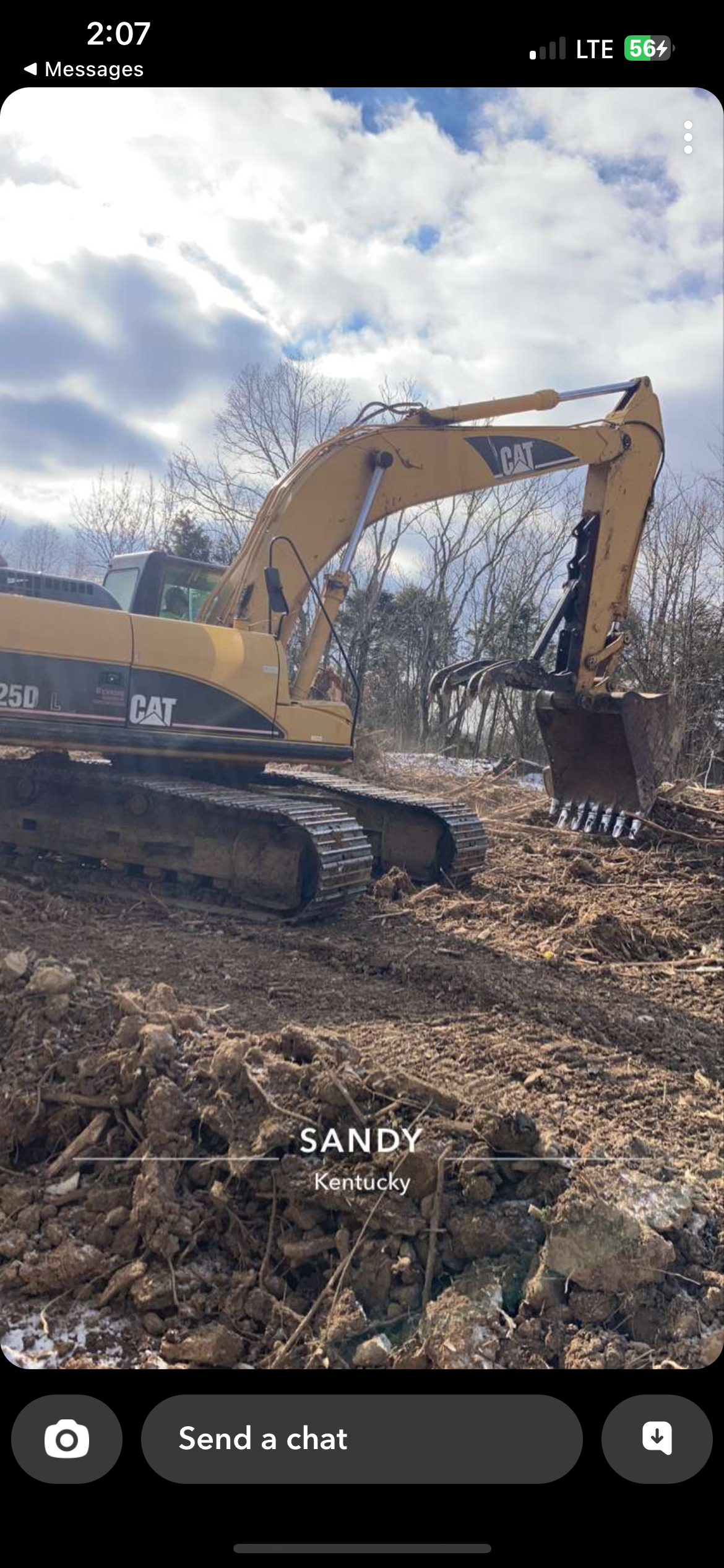 A yellow Caterpillar excavator sits on a muddy, dirt-covered construction site under a cloudy sky.