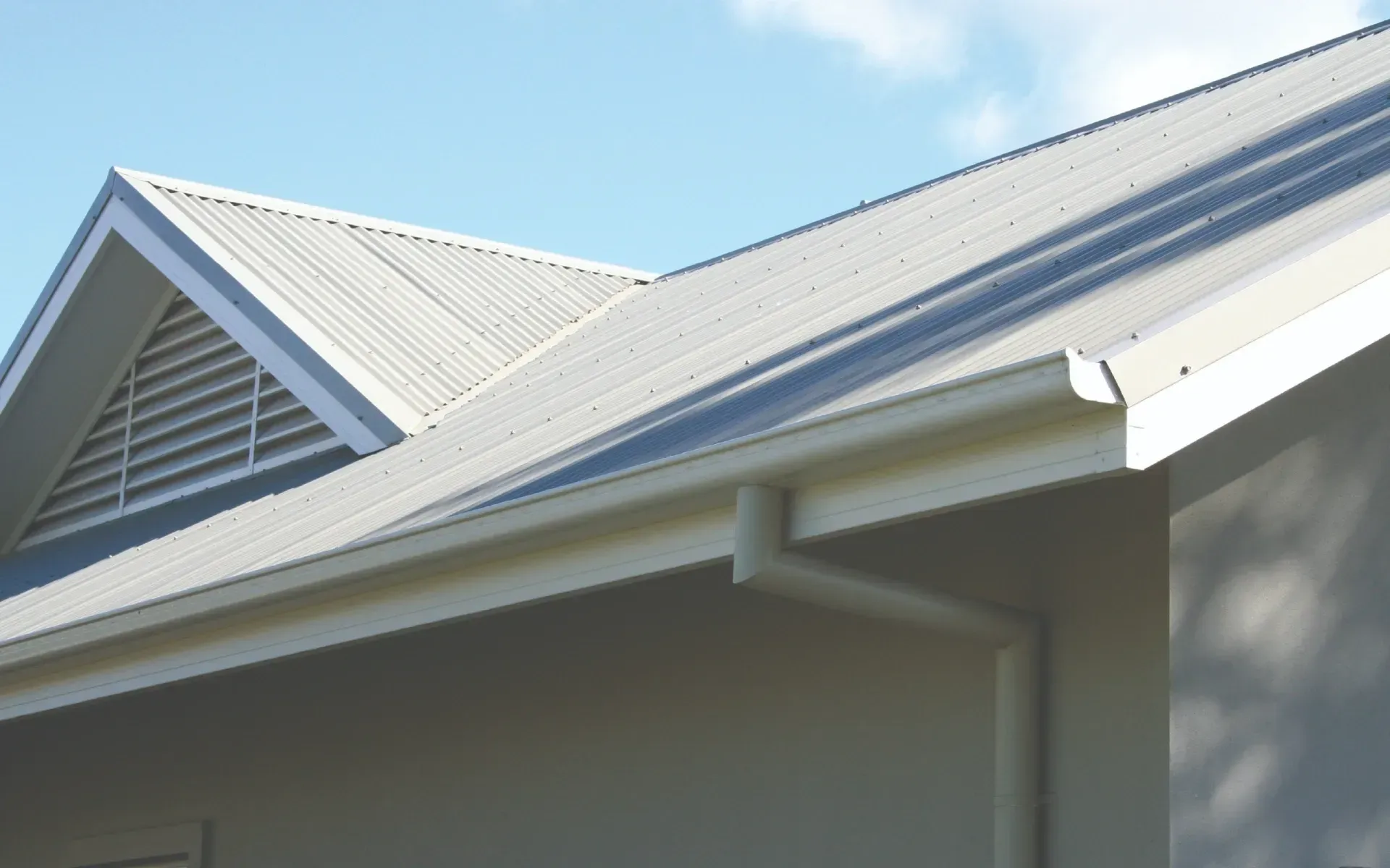 White metal roof and gray house exterior against a blue sky