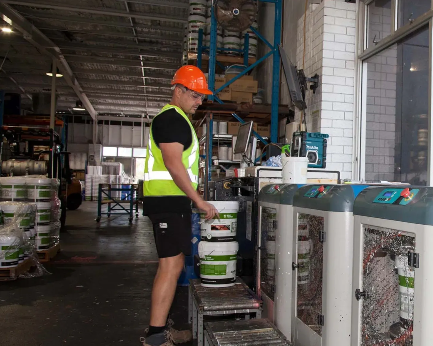 Worker in orange hard hat operating machinery in an industrial warehouse setting