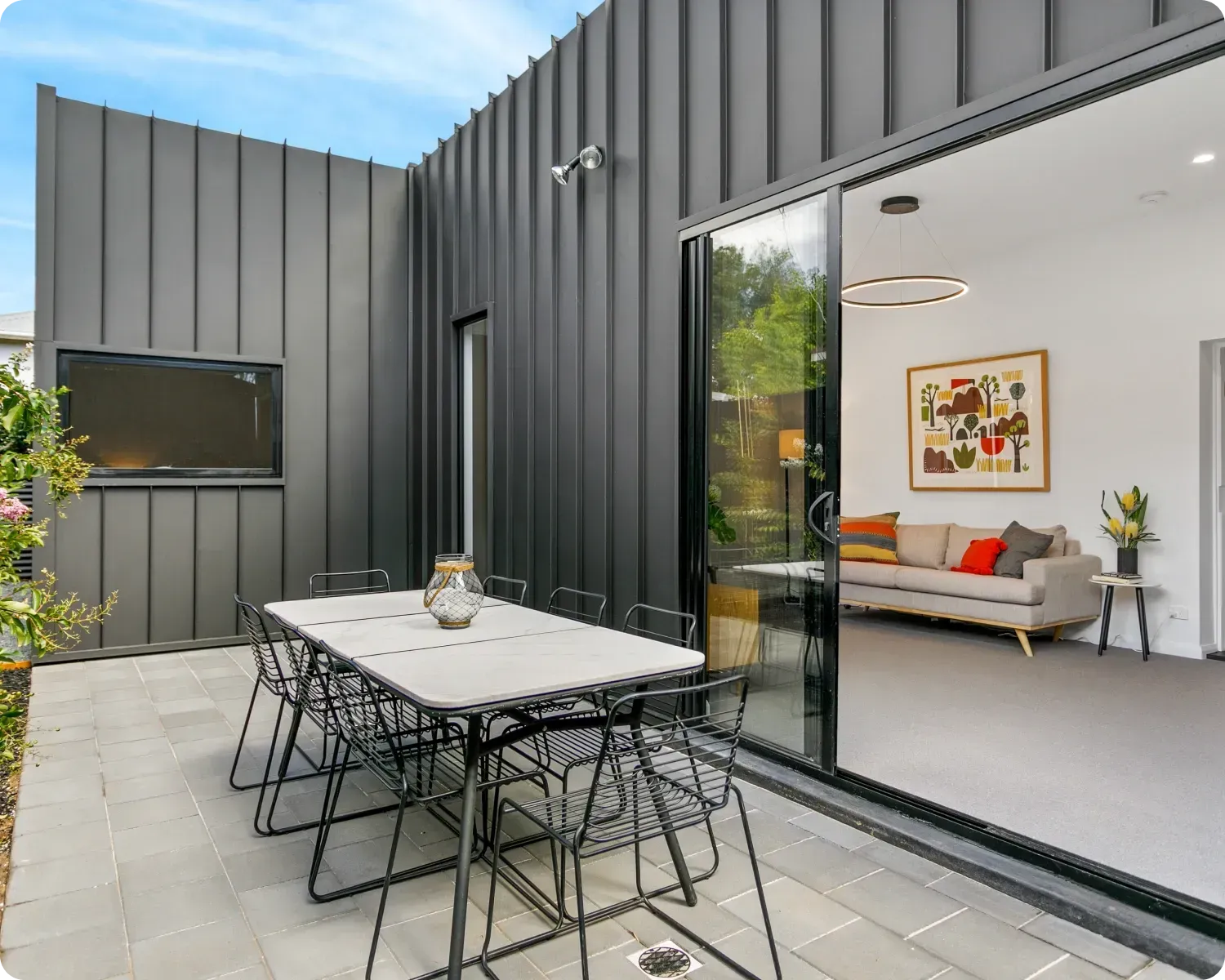 Modern patio with outdoor dining table beside a sliding glass door to a bright living room