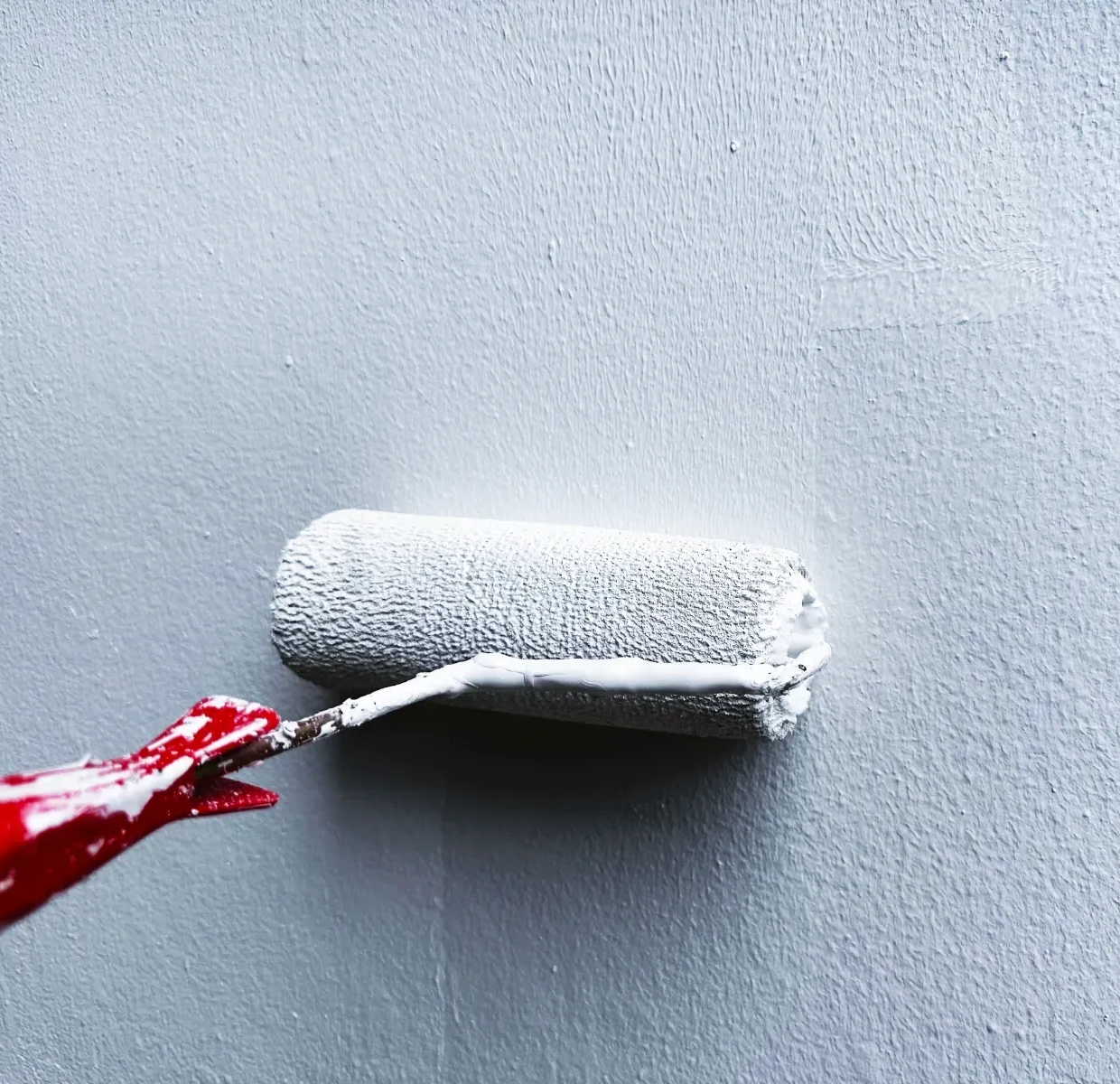 Paint roller applying white paint on a light gray wall
