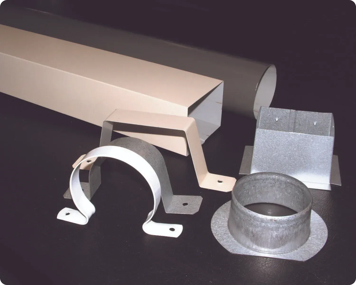 Assorted metal brackets and straps, including a curved silver band and gray sheet-metal pieces on a dark surface