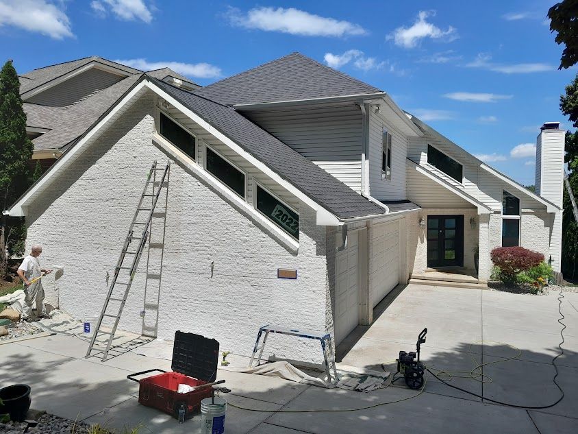 A man is painting the side of a house with a ladder.