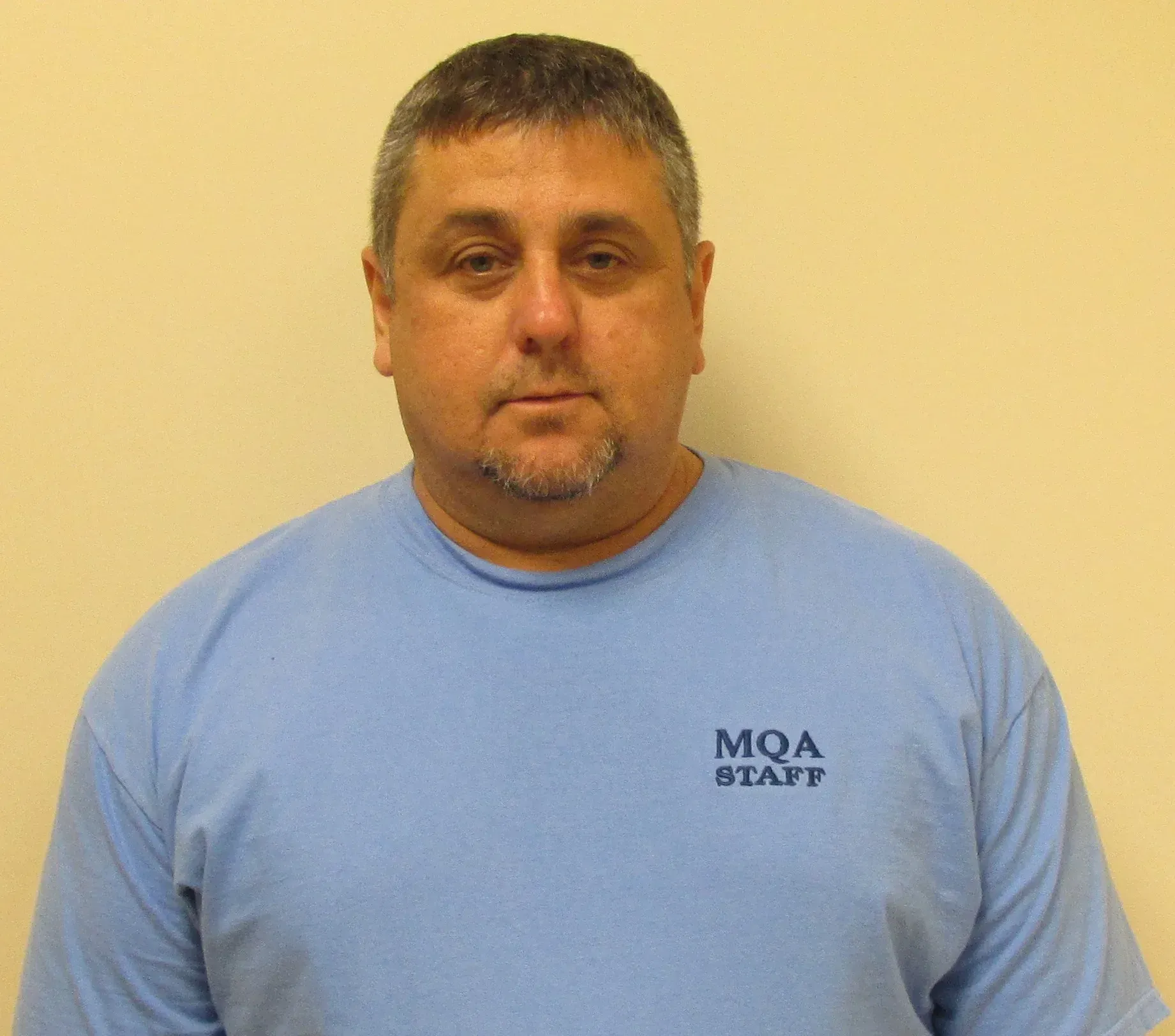 Man in a light blue shirt against a beige wall, facing the camera.