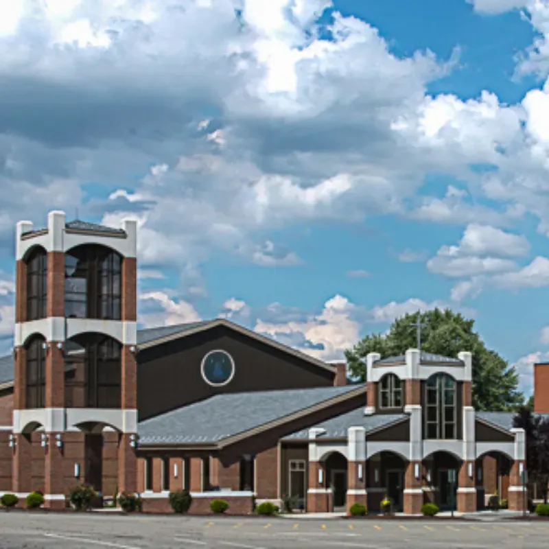 Brick church with twin towers and white trim under a partly cloudy blue sky