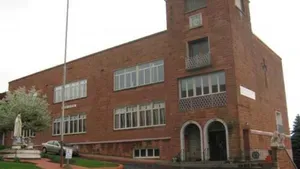 Red brick building with tall tower, arched entrance, and rows of windows on a cloudy day