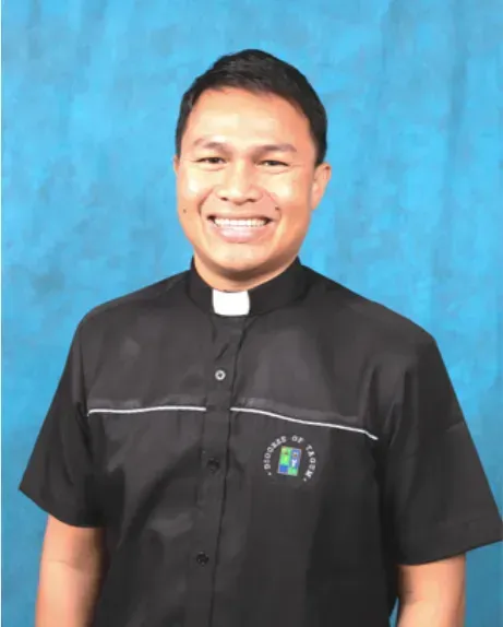 Portrait of a smiling priest in a black clerical shirt with white collar against a blue backdrop