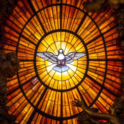 Stained glass dove with outstretched wings glowing in a circular golden-orange sunburst