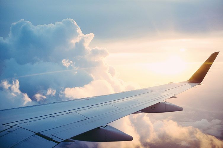the wing of an airplane is flying through the clouds at sunset .