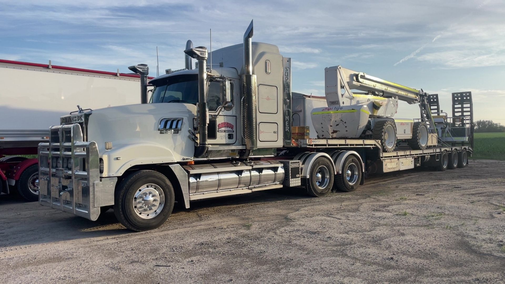 White Semi-Truck with Crane Trailer Parked on A Gravel Lot — Rainbow and Sons Heavy Haulage in Coffs Harbour, NSW