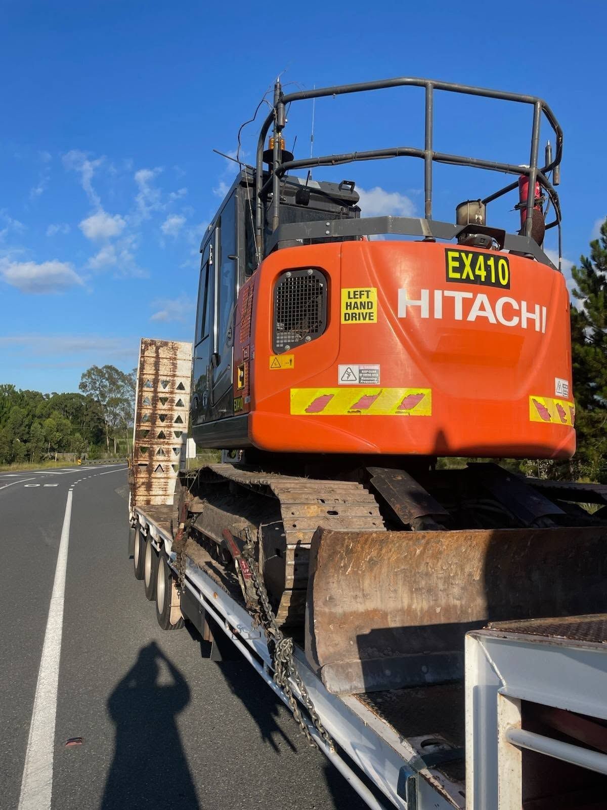 Orange Hitachi EX40 excavator strapped on a flatbed truck under a blue sky — Rainbow and Sons Heavy Haulage in Wells Crossing, NSW