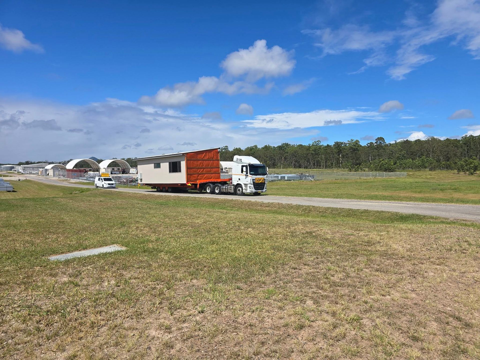 Truck with Red Container Driving on A Grassy Field Under a Blue Sky — Rainbow and Sons Heavy Haulage in Wells Crossing, NSW