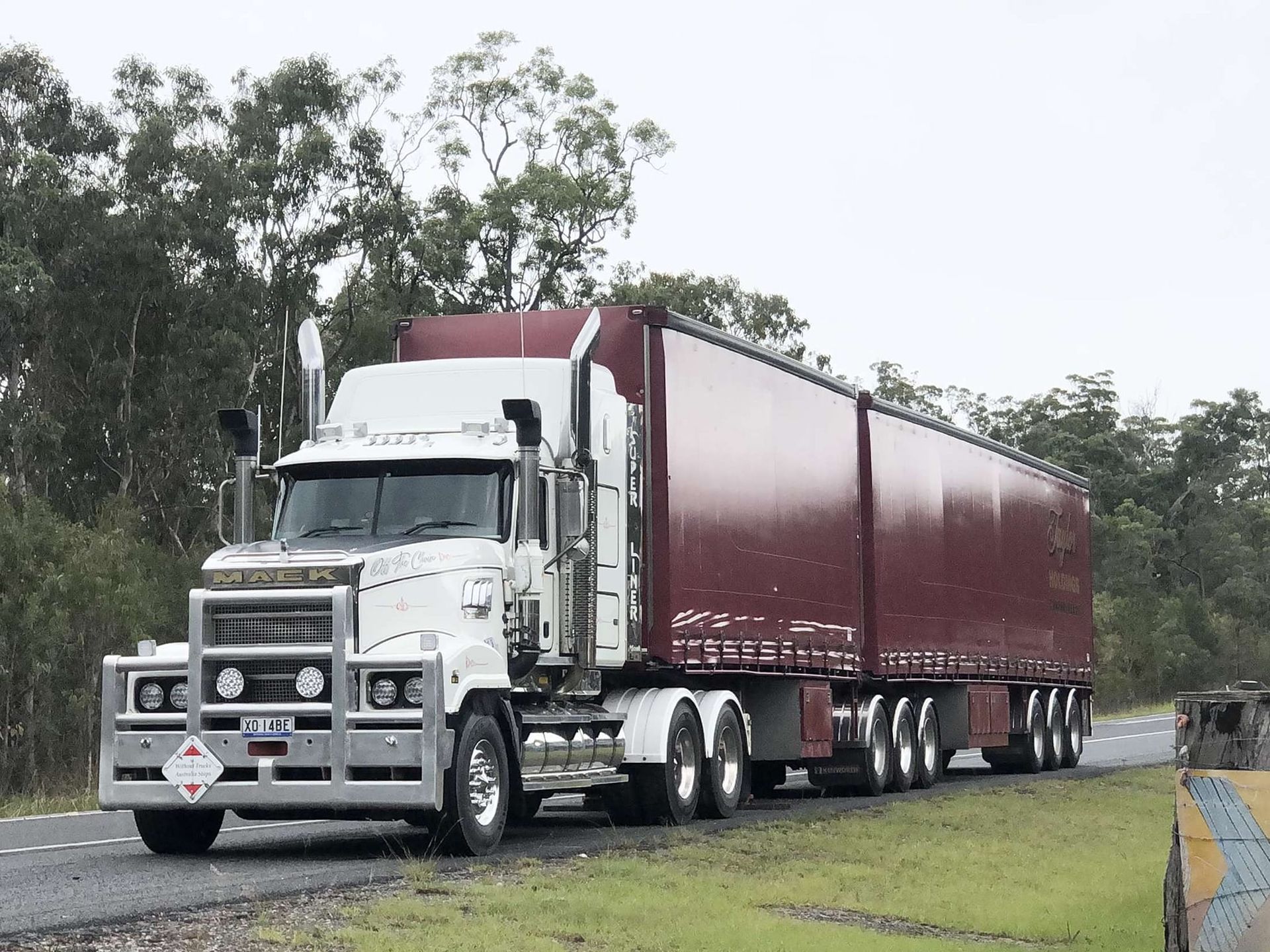 White Semi-Truck Hauling a Maroon Trailer on A Road — Rainbow and Sons Heavy Haulage in Wells Crossing, NSW