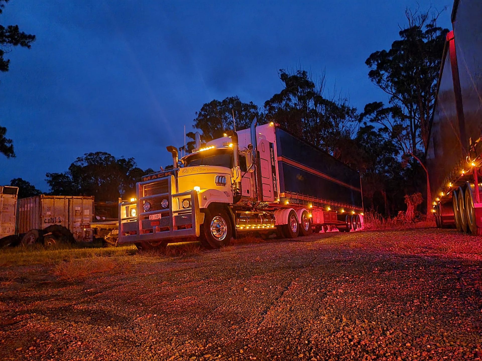 Tow Truck with Flashing Lights Parked on A Gravel Lot at Dusk — Rainbow and Sons Heavy Haulage in Wells Crossing, NSW