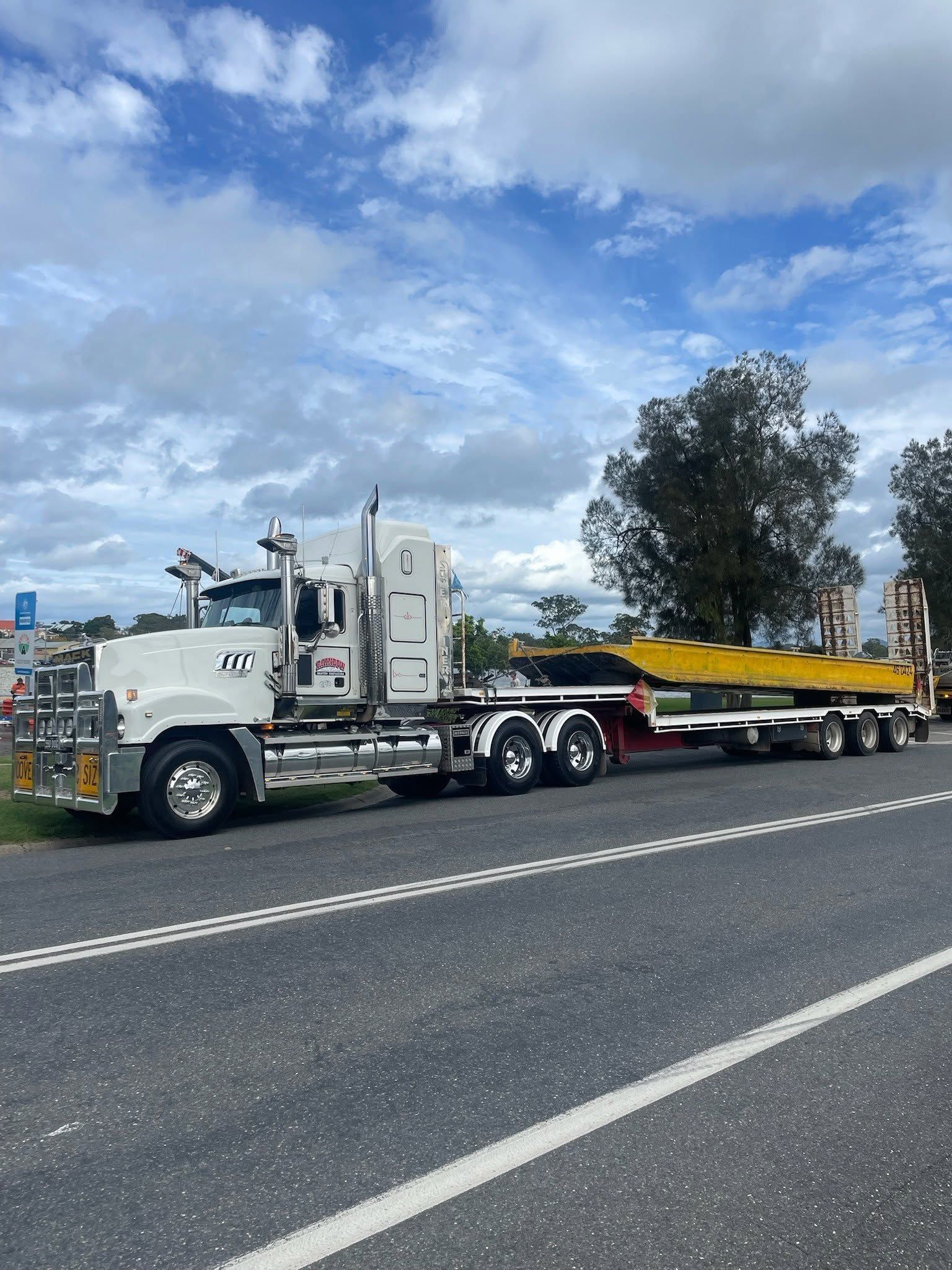White Semi-Truck Hauling a Long Yellow Flatbed Trailer on A Highway — Rainbow and Sons Heavy Haulage in Wells Crossing, NSW