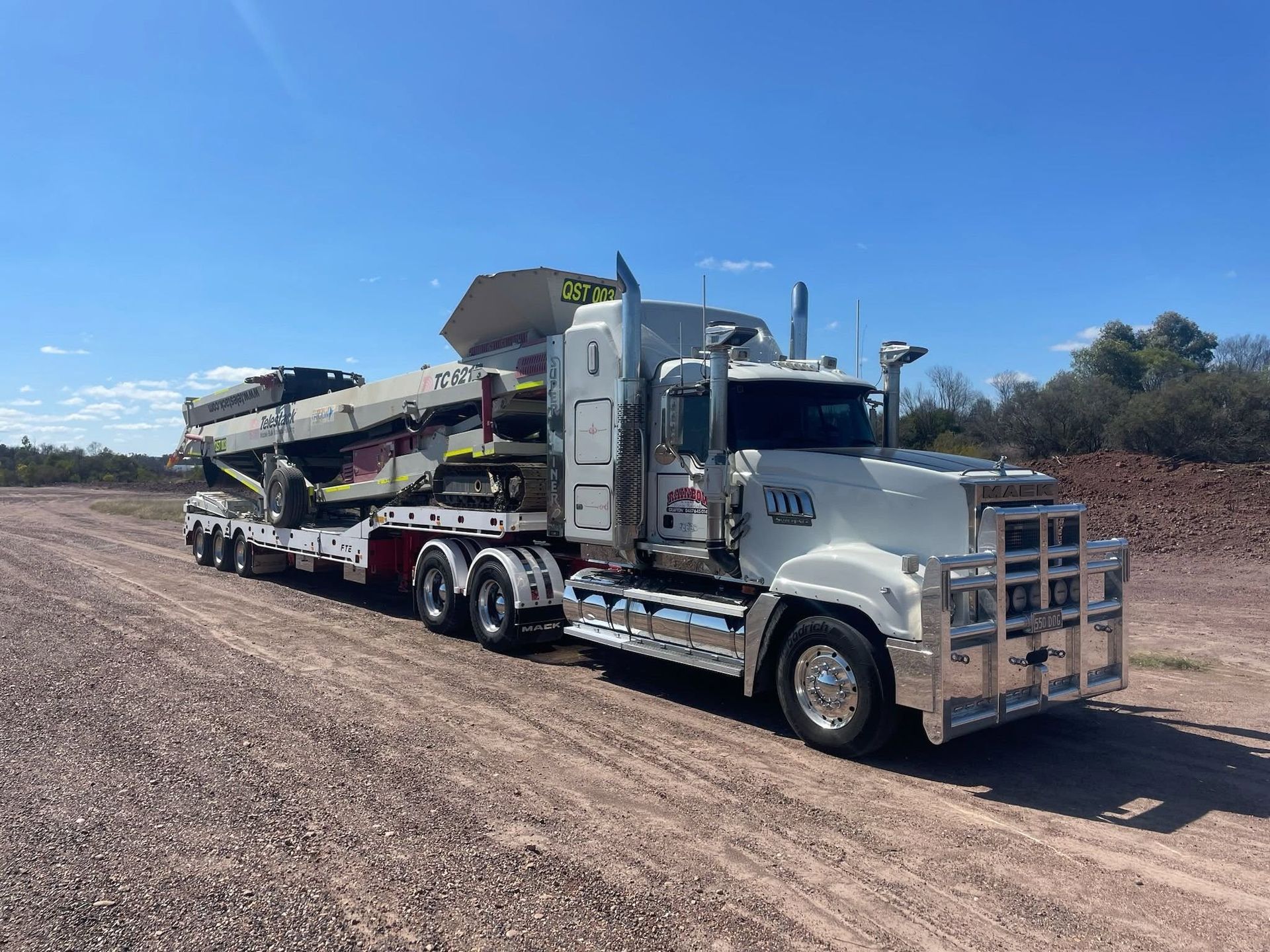 White Semi-Truck Hauling Construction Machinery on A Dirt Road — Rainbow and Sons Heavy Haulage in Wells Crossing, NSW